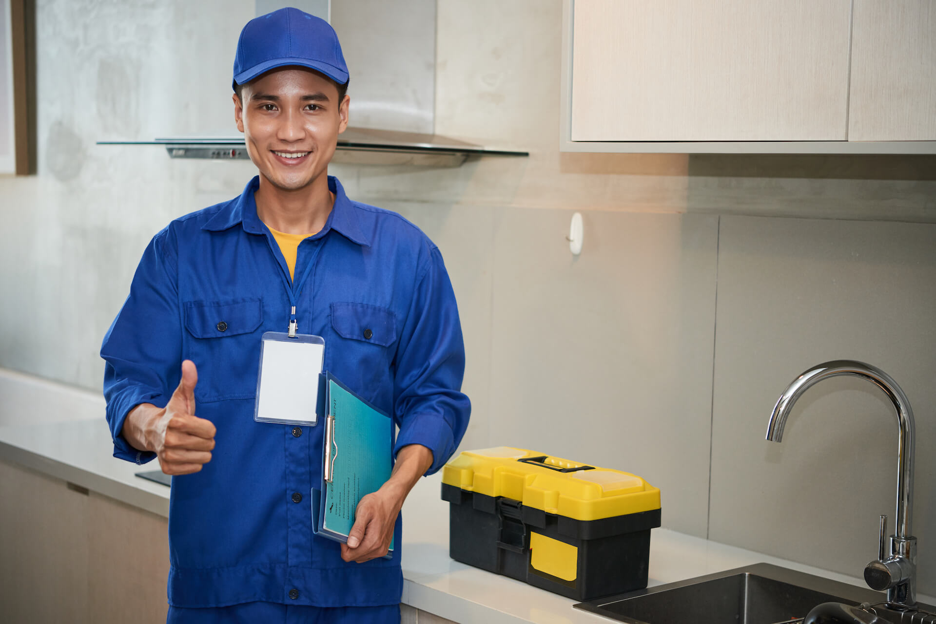 cheerful-asian-plumber-standing-near-kitchen-sink-showing-thumb-up